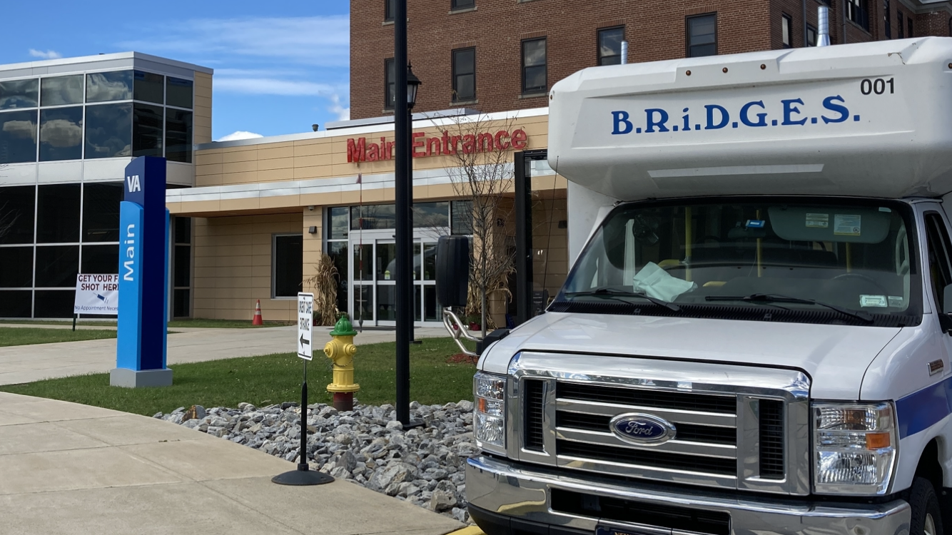 A small accessible bus with the word BRIDGES on it, it is in front of a hospital.